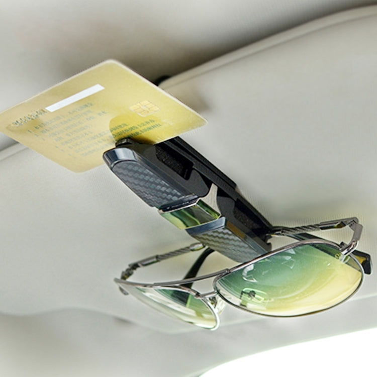 Vehicle mounted glasses clip with black carbon-fiber strap holding eyeglasses