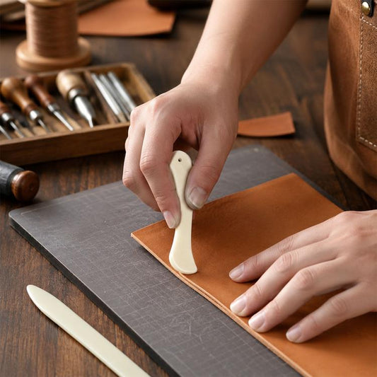 Bone-colored craft scraper tool in hand, used to burnish and crease leather