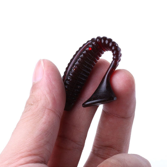 Soft screw-tail fishing lure held between fingers, dark red with ribbed body