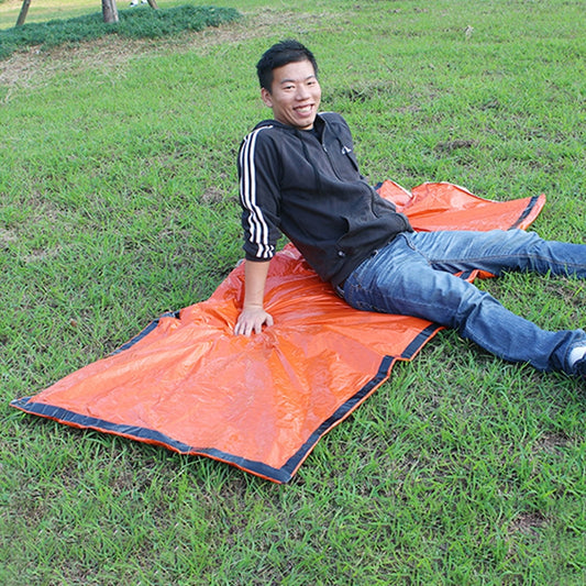 Orange thermal envelope sleeping bag laid on grass, with black trim and hooded opening