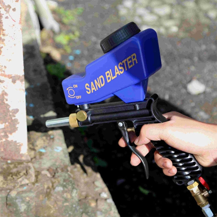 Blue sand blaster gun held in hand with nozzle spraying over outdoor surface