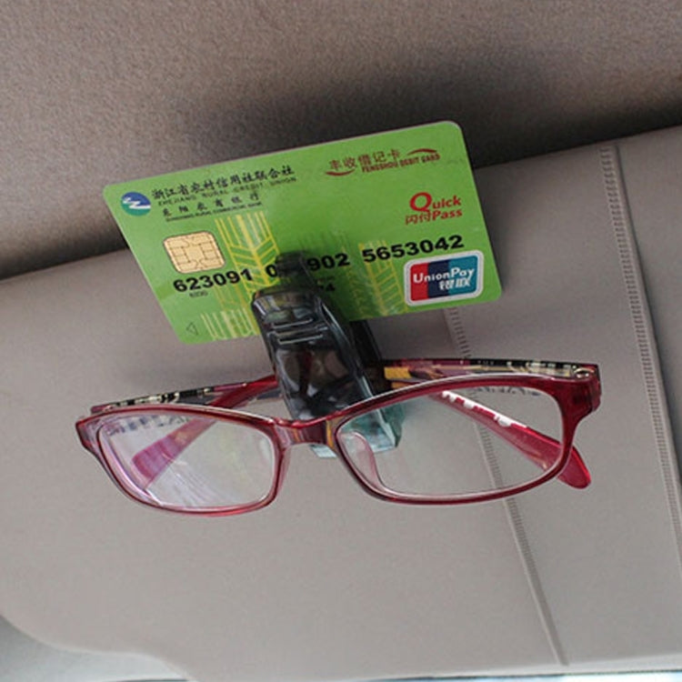 Black sunglass clip mounted on car visor holding a business card