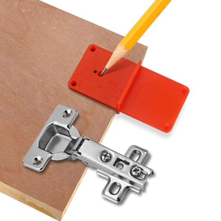 Orange hinge positioner template with silver hinge kit and pencil tip over wood