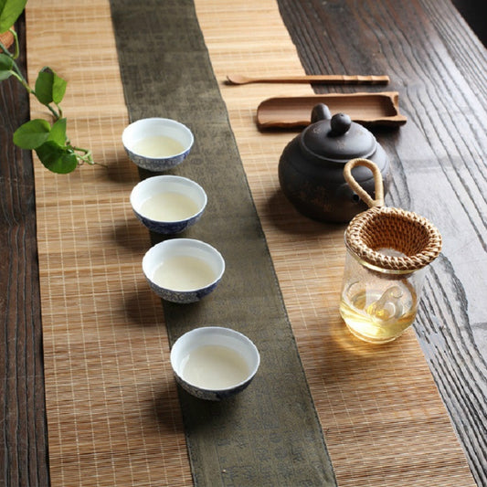 Rattan tea strainer with basket bowl and handle, beside tea cups and kettle