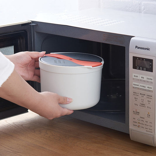 White rice steamer pot with orange lid held in an open microwave