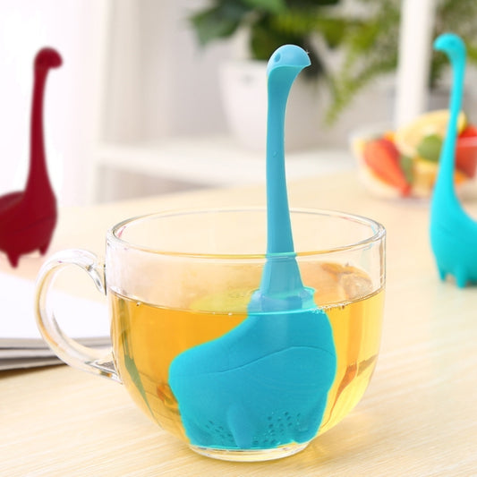 Blue dinosaur tea infuser strainer with handle, resting in a glass teacup.