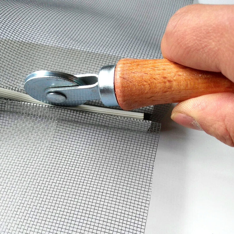 Window spline roller tool held by hand, metal wheel rolling on wire screen mesh