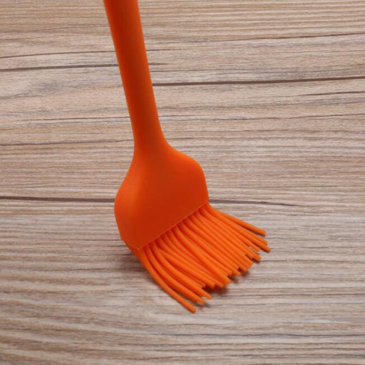 Orange silicone basting brush with fan-shaped bristle head and long handle.