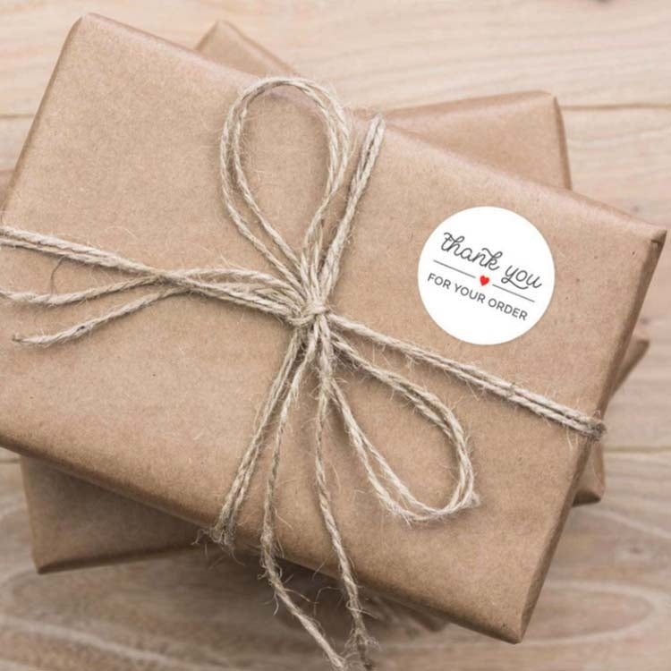 Round thank-you order sticker tied onto a kraft gift package with string