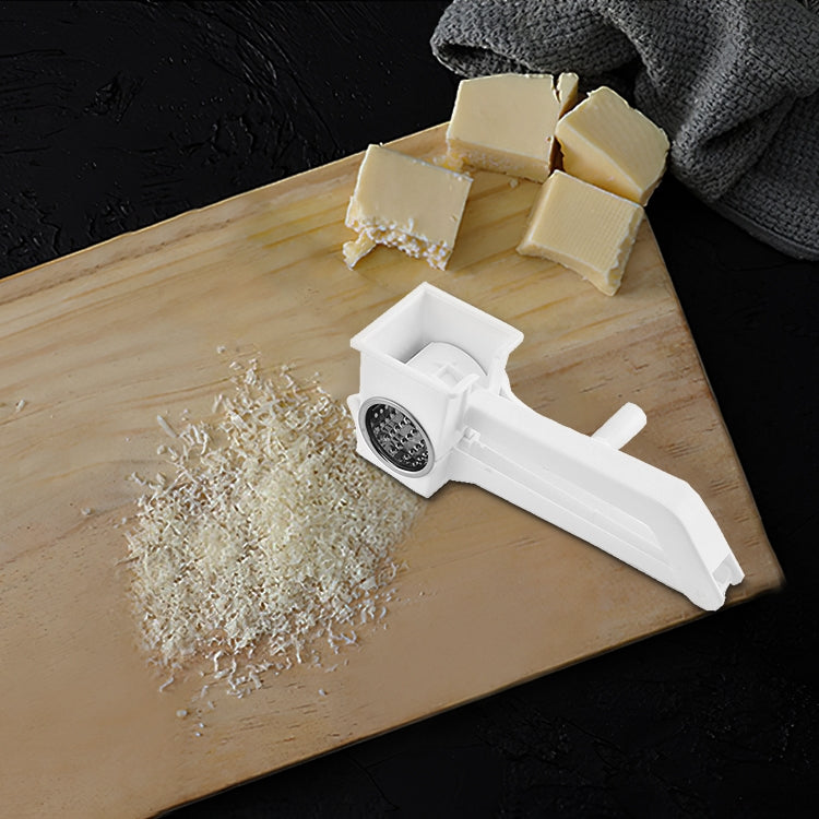 Plastic hand-crank rotary grater producing cheese shavings on cutting board