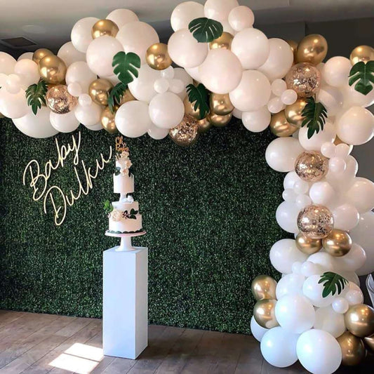 White and gold balloon garland arch with green leaf decals and confetti balloons