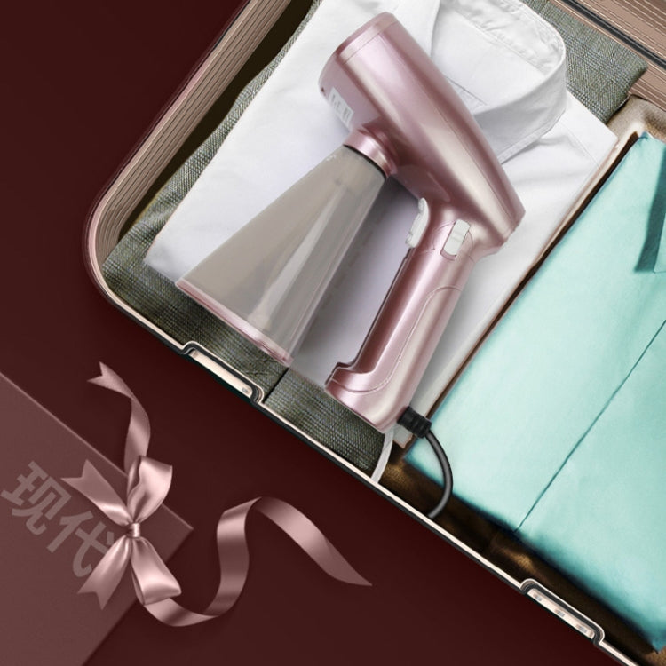 Rose-pink mini handheld garment steamer on folded fabric with connected power cord
