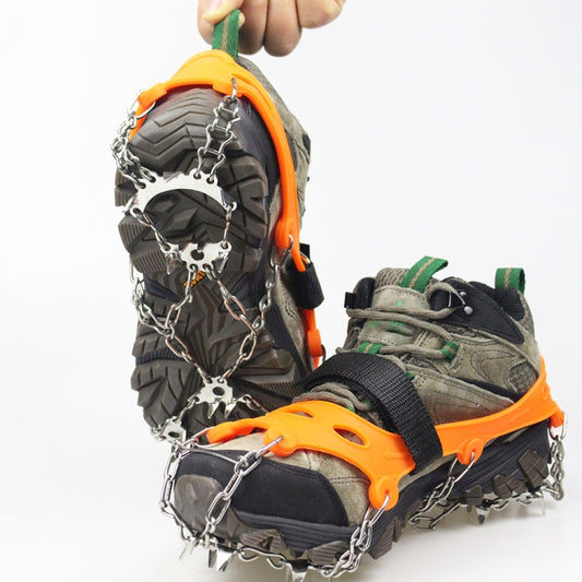Orange ice traction crampons with steel spikes on winter boots, chain links attached