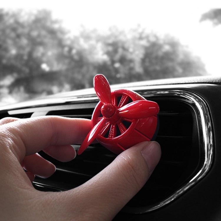 Red car air outlet perfume swivel fan held near car air vent