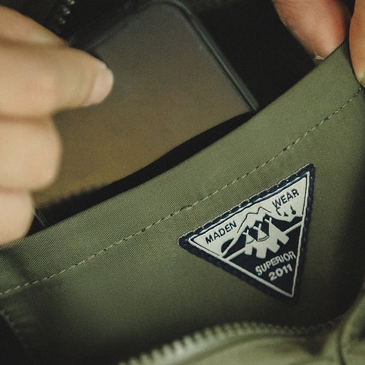 Green messenger bag close-up with stitched logo patch and zipper trim.