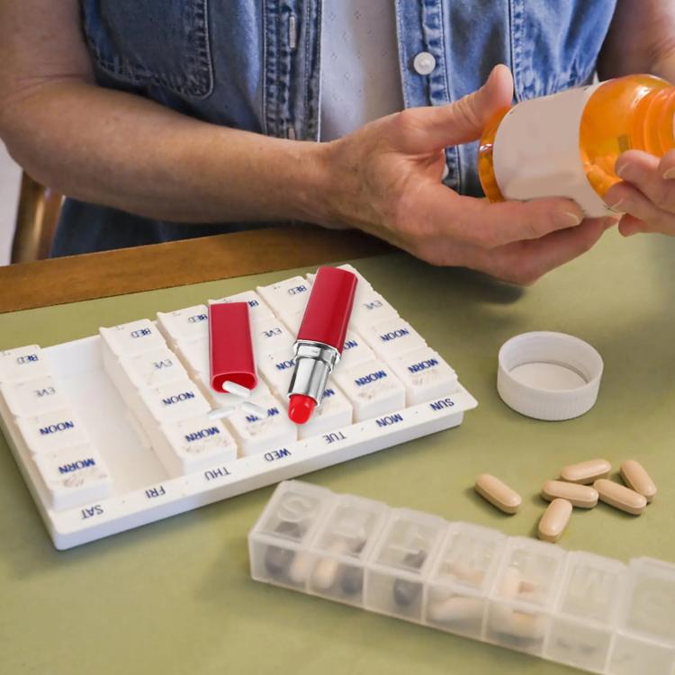 Red lipstick-shaped pillbox with cap off next to pills and blister cards.