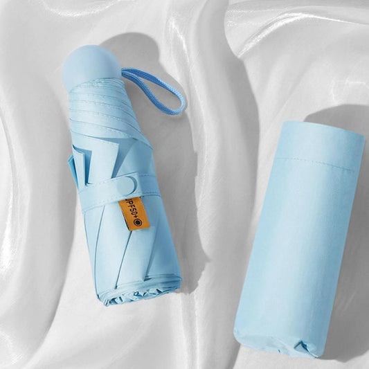 Light blue foldable capsule umbrella with matching strap, packed in compact sleeve.