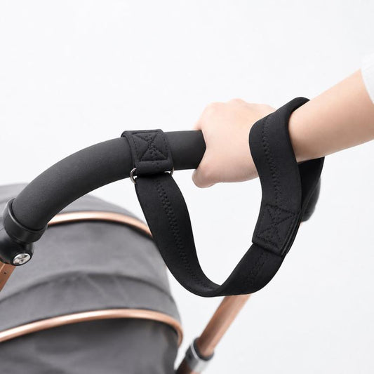Black stroller handlebar wrist safety strap with soft loop and metal ring, secured on hand.