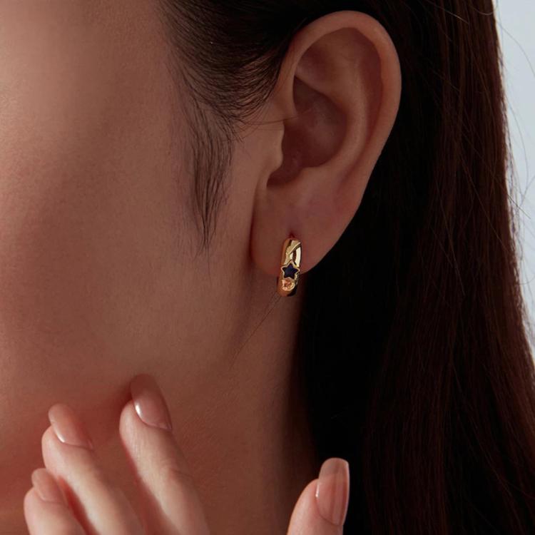 Gold-tone hoop earrings with blue star enamel worn on ear