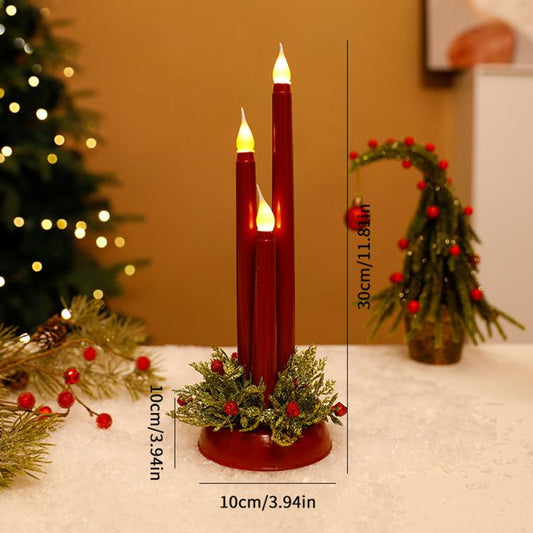 Two lit red LED taper candles with evergreen wreath and red berry accents on round base