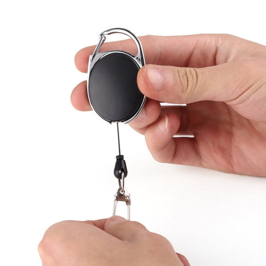 Retractable key ring holder with black oval case and metal loop, held by a hand.