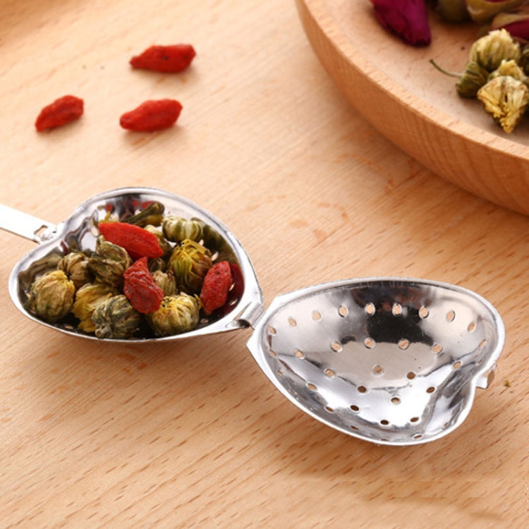 Two heart-shaped stainless tea infuser spoons filled with dried tea leaves