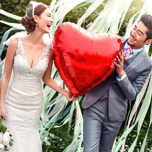 Red heart-shaped foil inflatable balloon, held by hands.