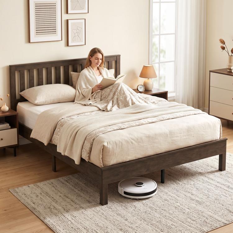 Walnut platform bed frame with slat headboard, bedding, and robot vacuum underneath
