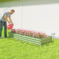 Light green galvanized raised garden bed with dense flower planting and gardener watering