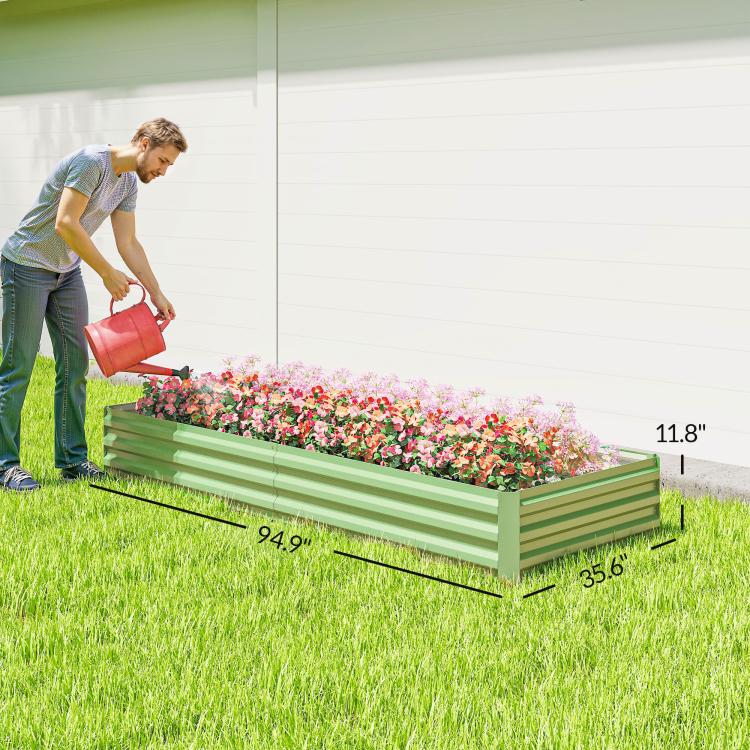 Light green galvanized raised garden bed with dense flower planting and gardener watering