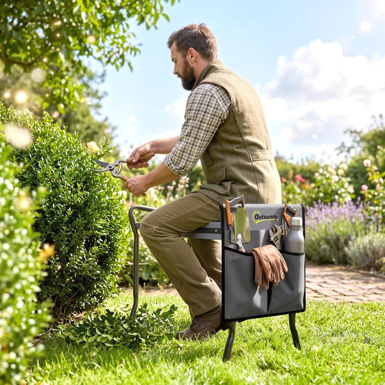 Gray garden seat with tool pouch on foldable steel frame while gardener trims plants.