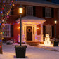 Outdoor black solar lantern post light standing in snow near a doorway and lights