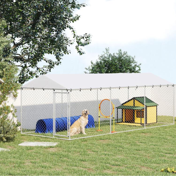 Outdoor dog kennel with silver chain-link walls and sloped roof in a backyard yard setting