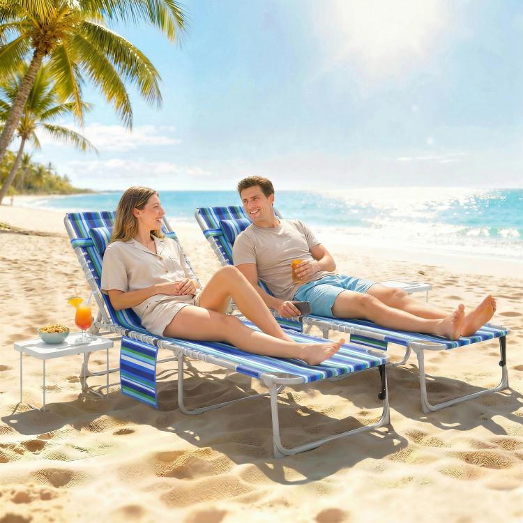 Pair of blue striped folding chaise lounge chairs with side tables on beach sand