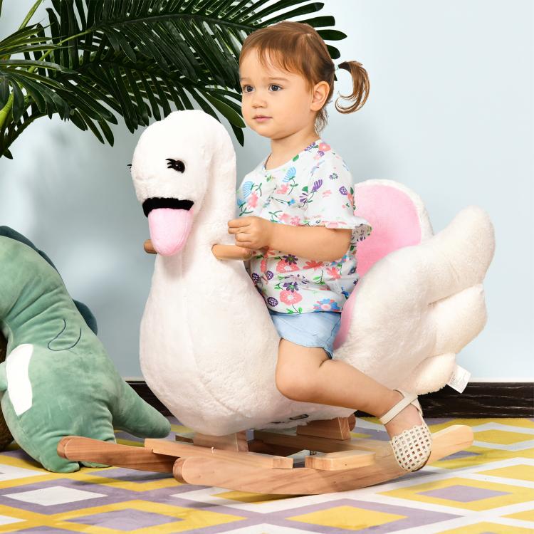 Toddler sitting on white plush swan rocking horse with pink padded seat