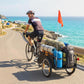 Bike cargo trailer with black frame and open bed, red safety flag, carrying bags while towing