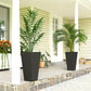 Two tall black outdoor plant pots on a stone patio with leafy plants