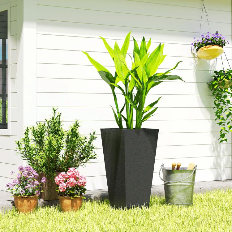 Tall black outdoor planter with green bamboo-like plant on grass near flowers