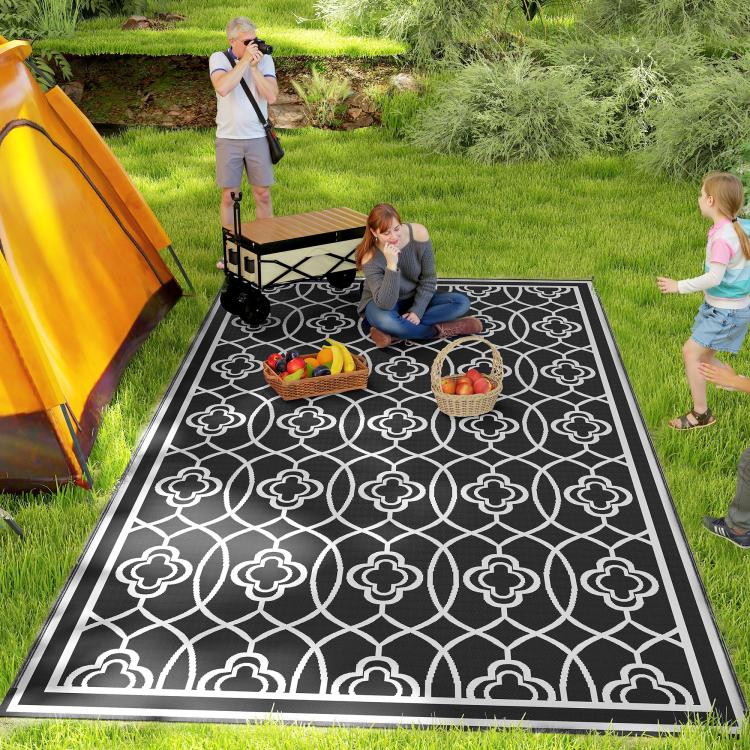 Outdoor reversible rug with black and white clover trellis pattern on grass