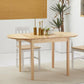 Natural wood drop-leaf dining table with a vase centerpiece and two chairs