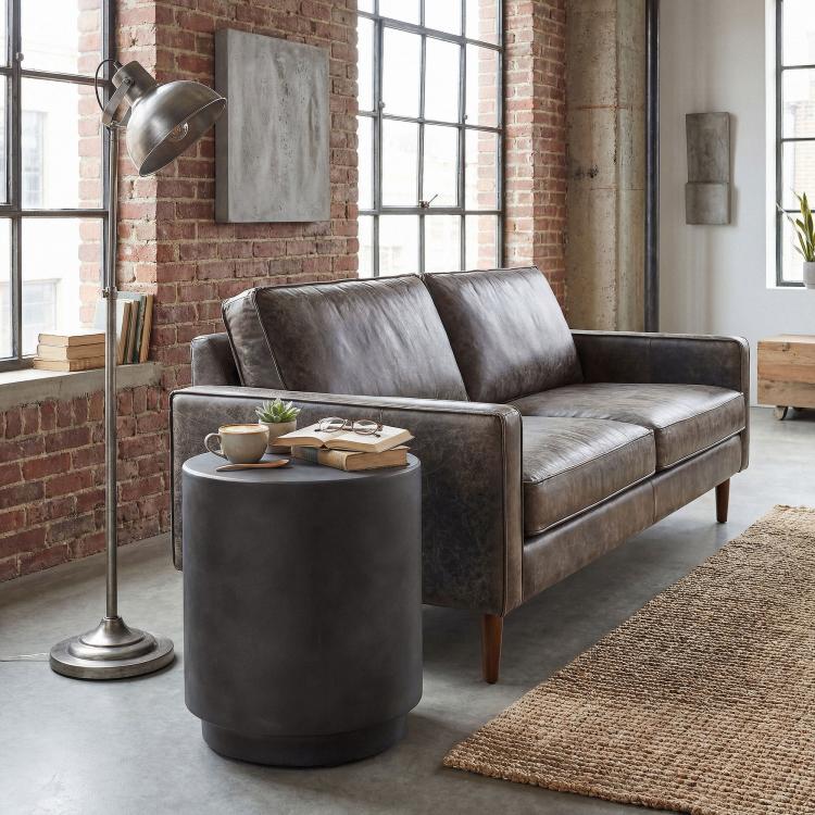 Dark gray cylindrical accent side table with concrete-look finish beside a sofa