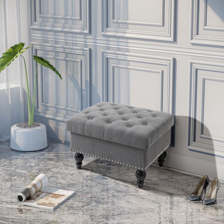 Gray storage ottoman bench with button-tufted lid, studded trim, and turned legs