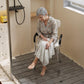 Shower bath chair with padded white seat, black armrests, and adjustable legs
