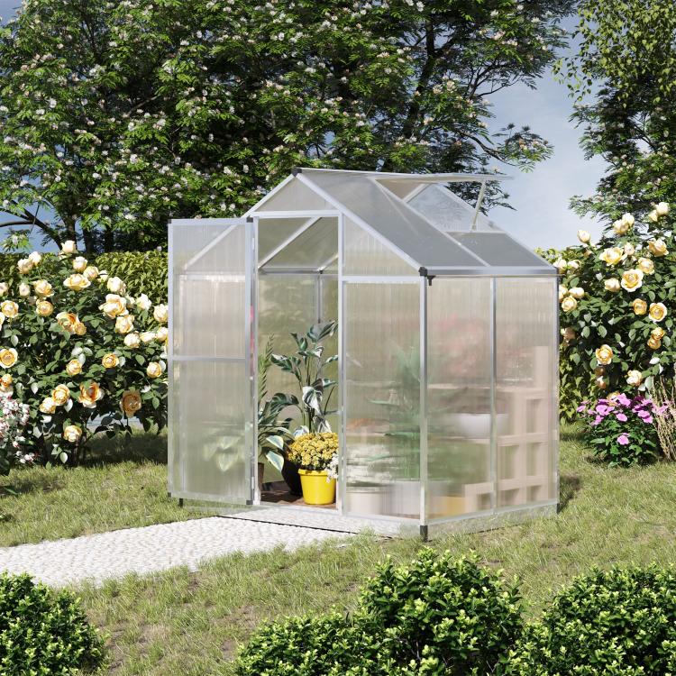 Walk-in polycarbonate greenhouse with clear walls and roof vent among flowers and shrubs