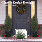 Two faux cedar trees in black textured pots beside a front door with wreath