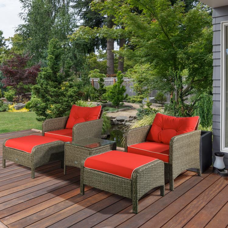 Outdoor rattan lounge chairs with red cushions and matching ottomans on a wooden deck