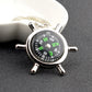 Silver compass-style keychain with black dial, green letters, and four metal spokes