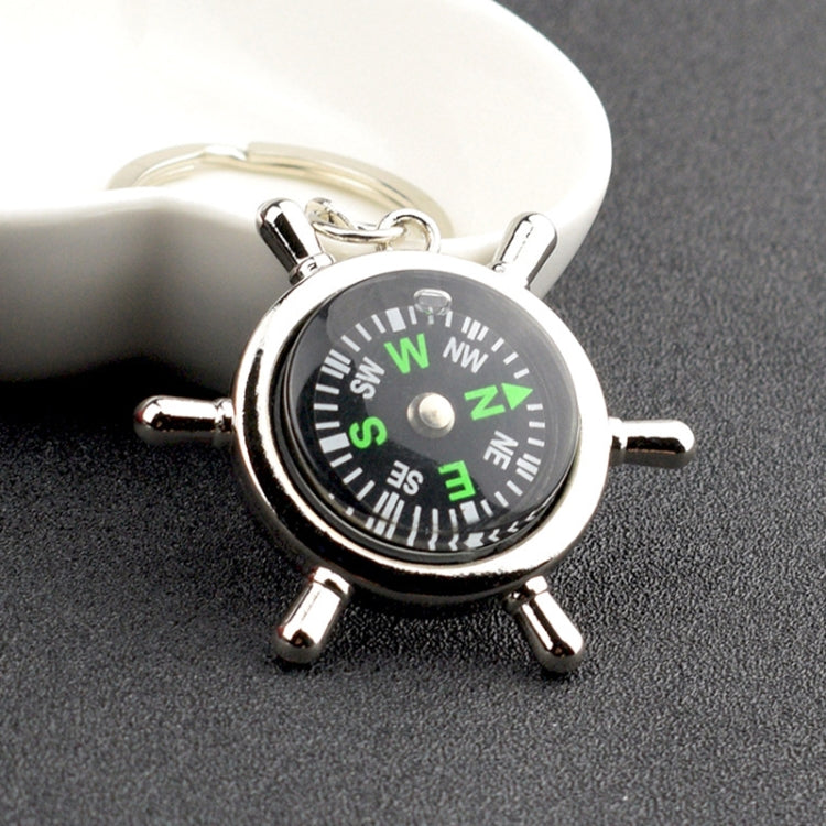 Silver compass-style keychain with black dial, green letters, and four metal spokes
