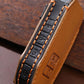 Leather key fob strap close-up, black center with orange stitching and embossed markings