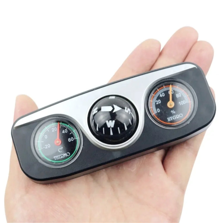 Handheld view of black car compass device with direction ball, thermometer, and hygrometer.